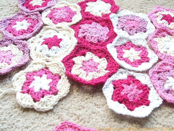 Close view of a pile of crocheted hexagons in white and pink colours.