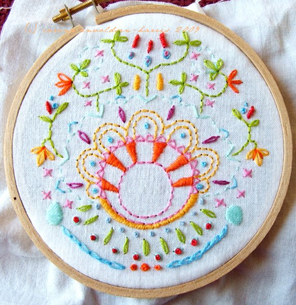 Overhead view of small embroidery hoop with multicolour embroidery on white fabric.