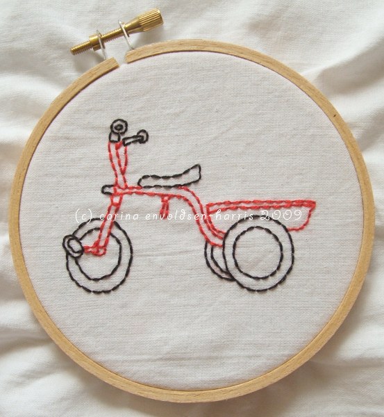 Black and red tricycle embroidered on white fabric.