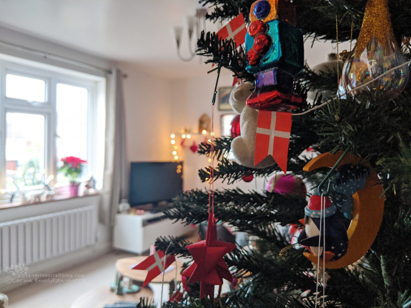 Decorated Christmas tree in half of the picture, in the background a tv and a window,