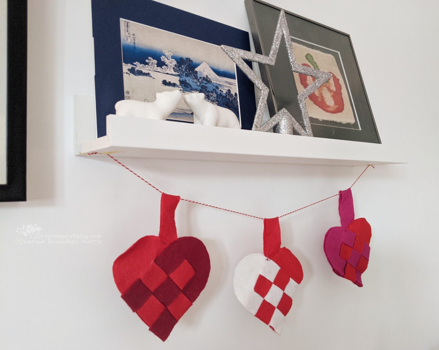 Picture shelf with pictures and polar bear ornaments. Felt woven hearts hanging from the shelf.
