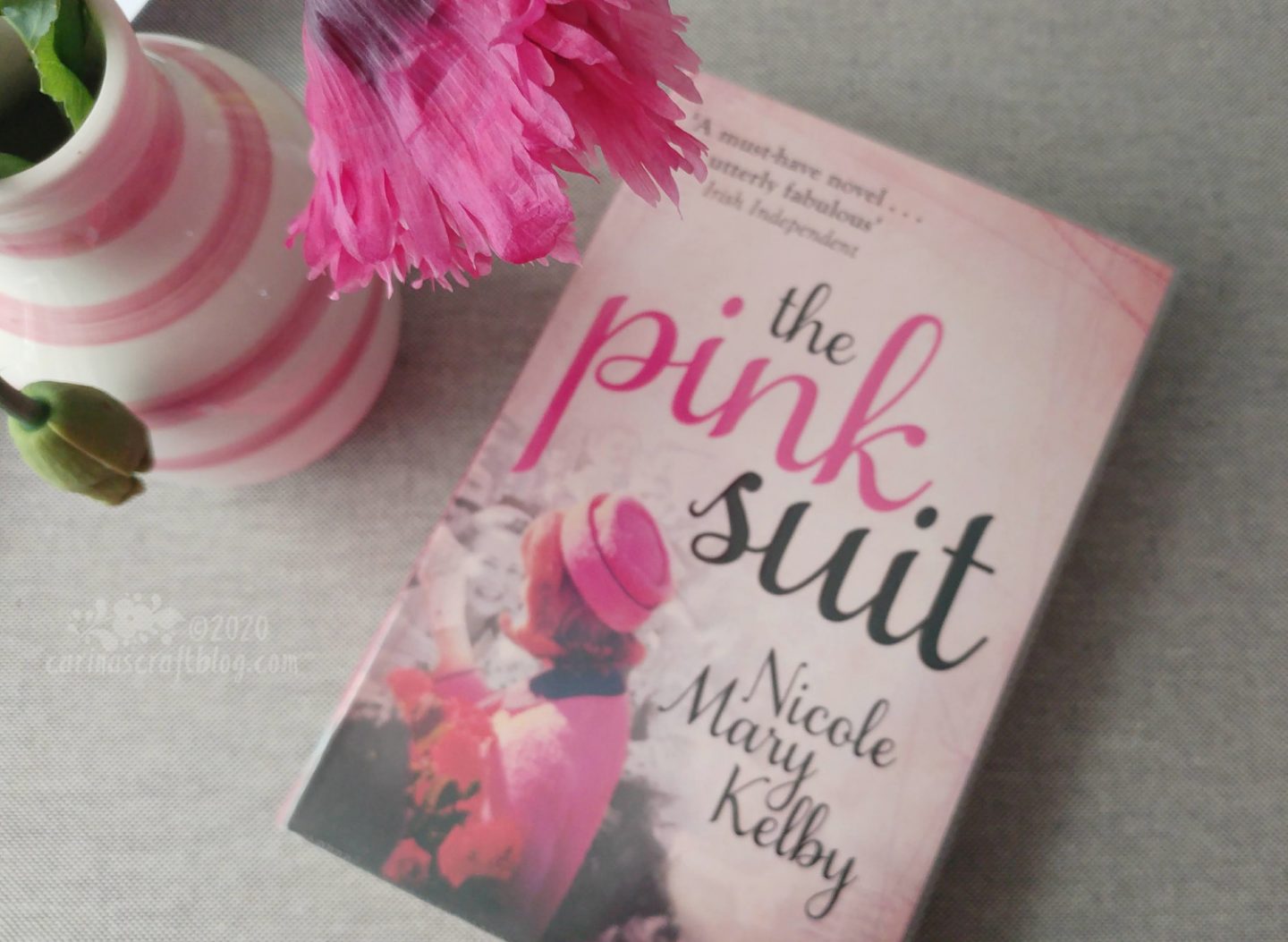 Book The Pink Suit next to a vase with a pink poppy.