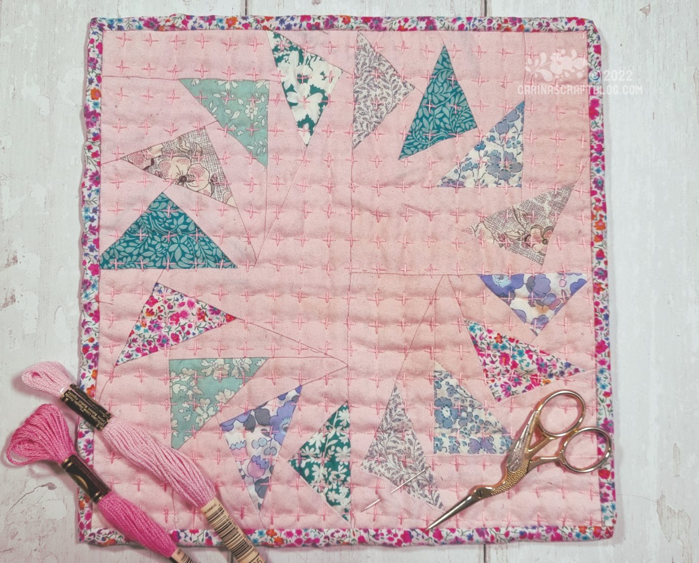 Overhead view of a mini quilt made from four small blocks of triangles set in a pink background. The four blocks together form a circle of triangles.
