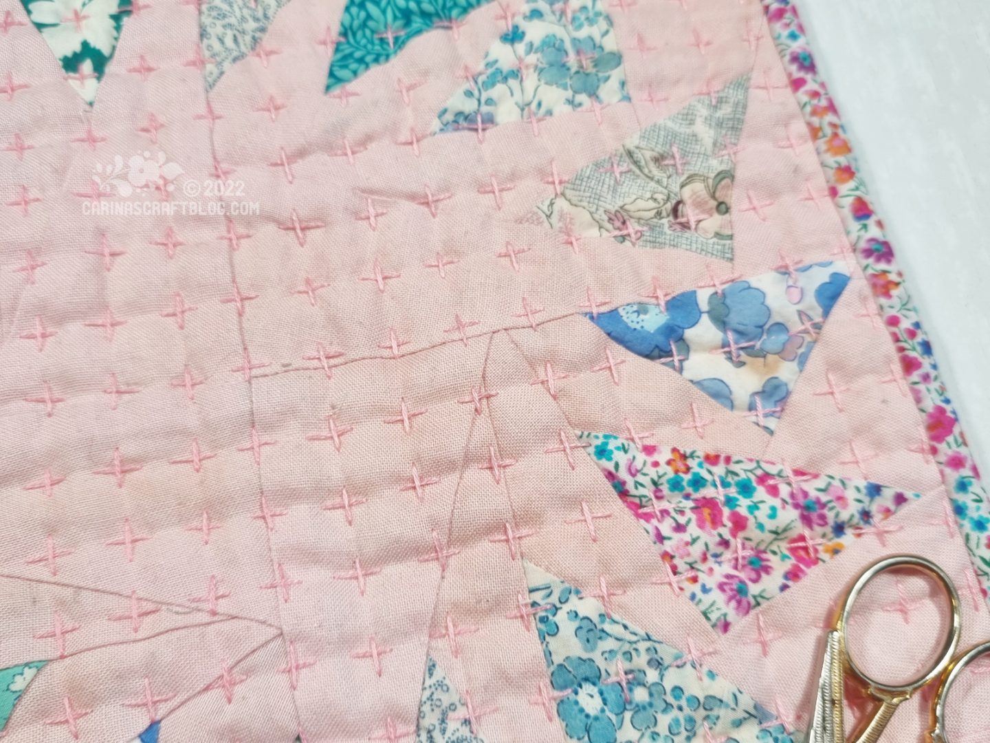 Close view of mini quilt with triangles on a pink background. Part of the fabric is lightly stained.