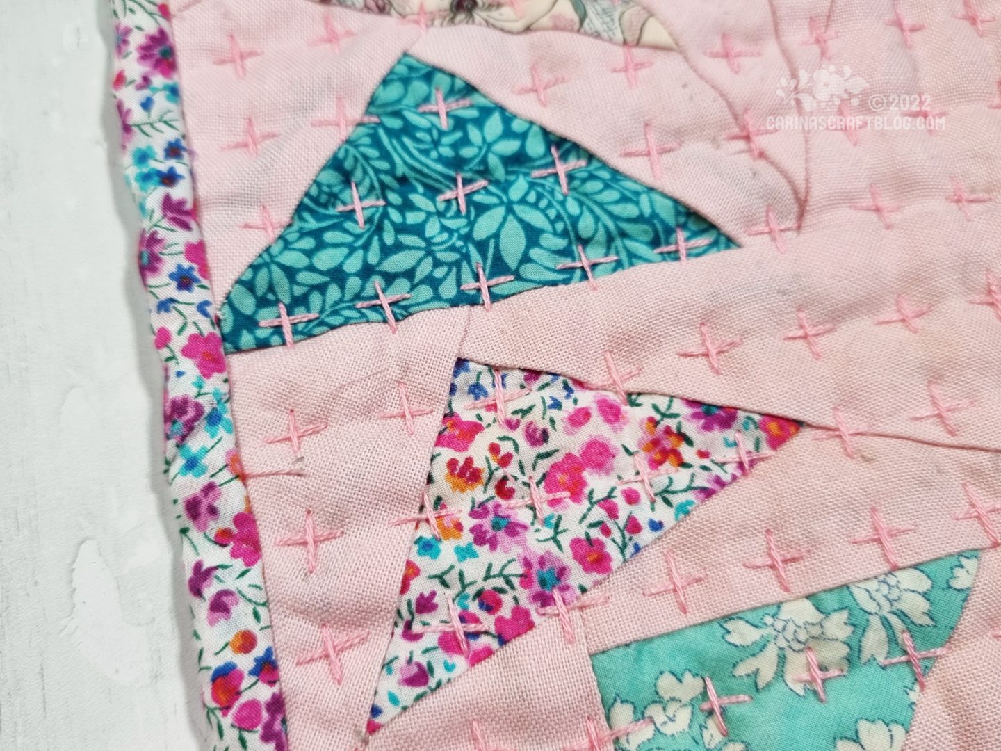 Close up of detail of mini quilt. Triangles of small pattern fabrics are set in a pink background fabric.