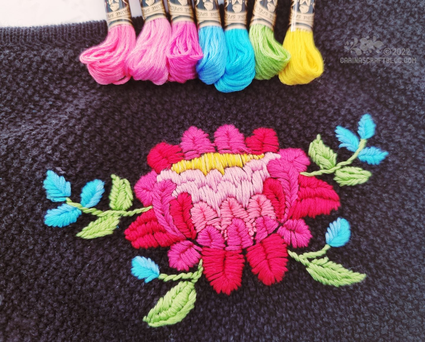 Folk art style flower in red and pink embroidered on a black cardigan.