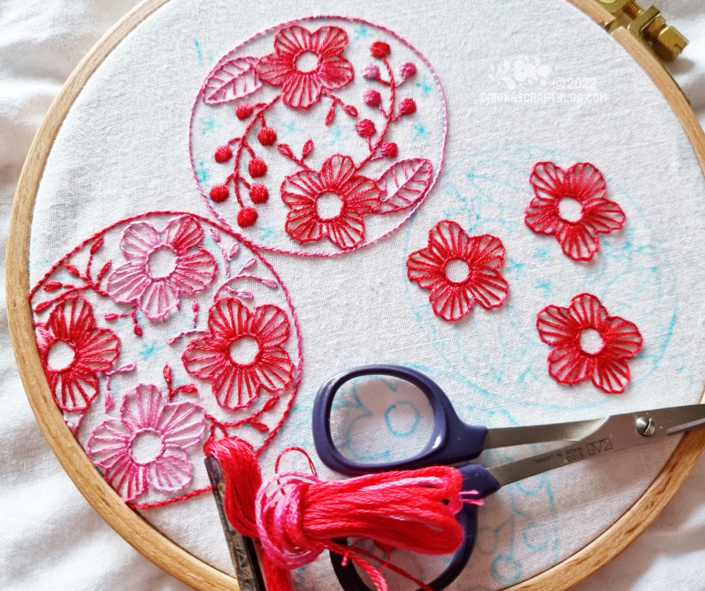 Closely cropped photo of an embroidery hoop with white fabric. On the fabric is embroidered round motifs with flowers in a variegated pink thread colour.