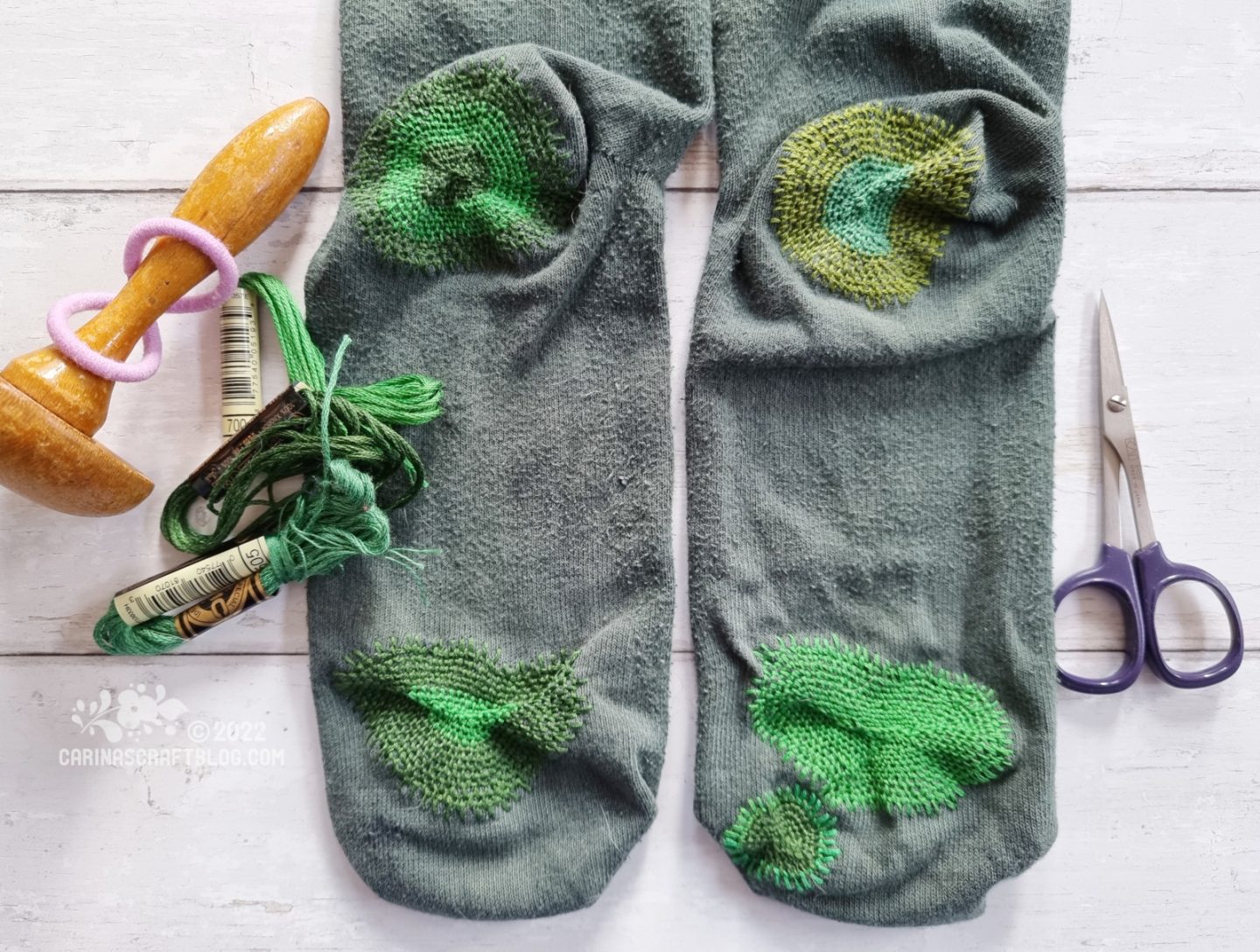 A pair of dark green socks with large darns on the bottom of both heels and toes in matching green colours.