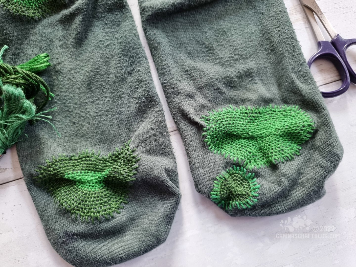 Close view of a pair of dark green socks with large darns on the bottom in matching green colours.