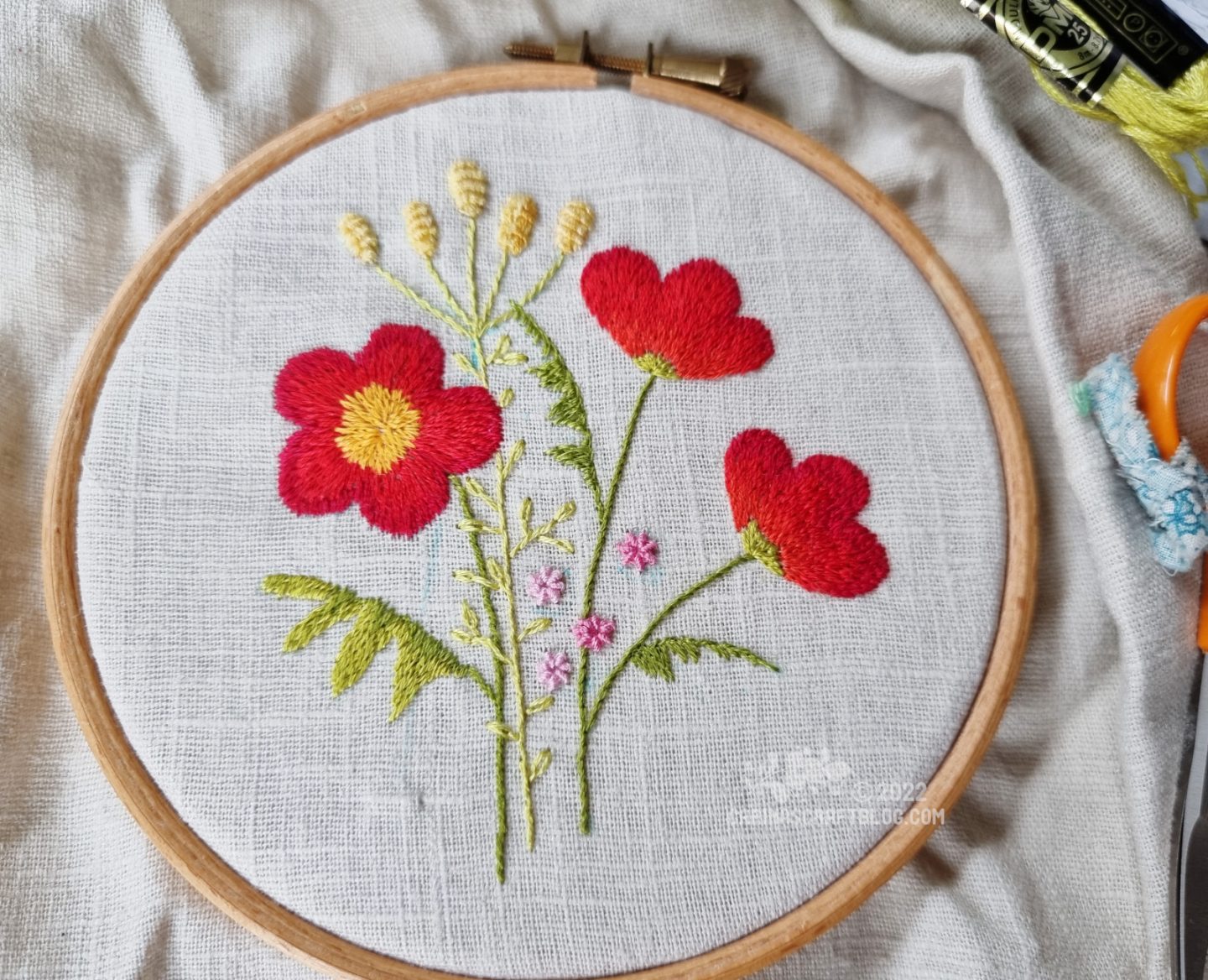 Embroidery hoop seen from above. In the hoop is linen fabric embroidered with red flowers.