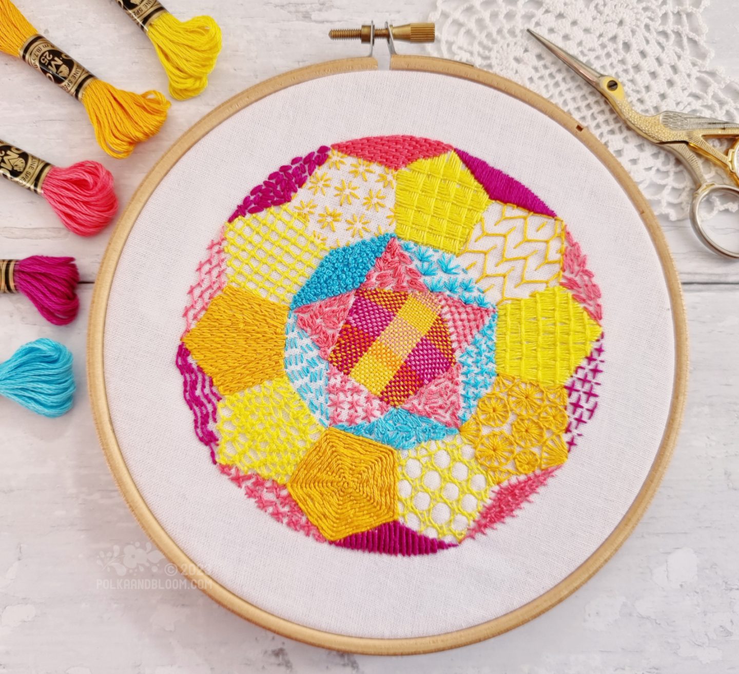 View from above of an embroidery hoop with white fabric. There is a round design embroidered on the fabric. The circle is divided into 31 segments, starting with a pentagon in the centre.