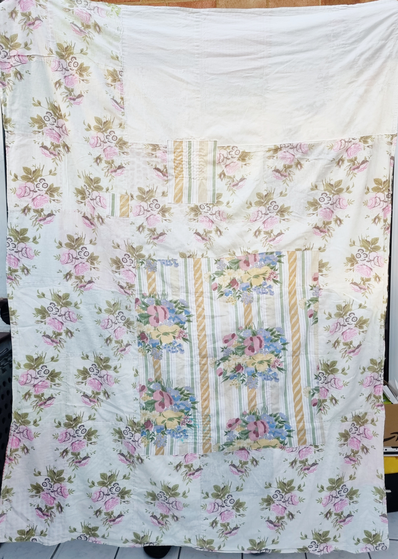 Full view of the back of a blanket, made from a floral duvet cover. There are several large patches on the fabric.