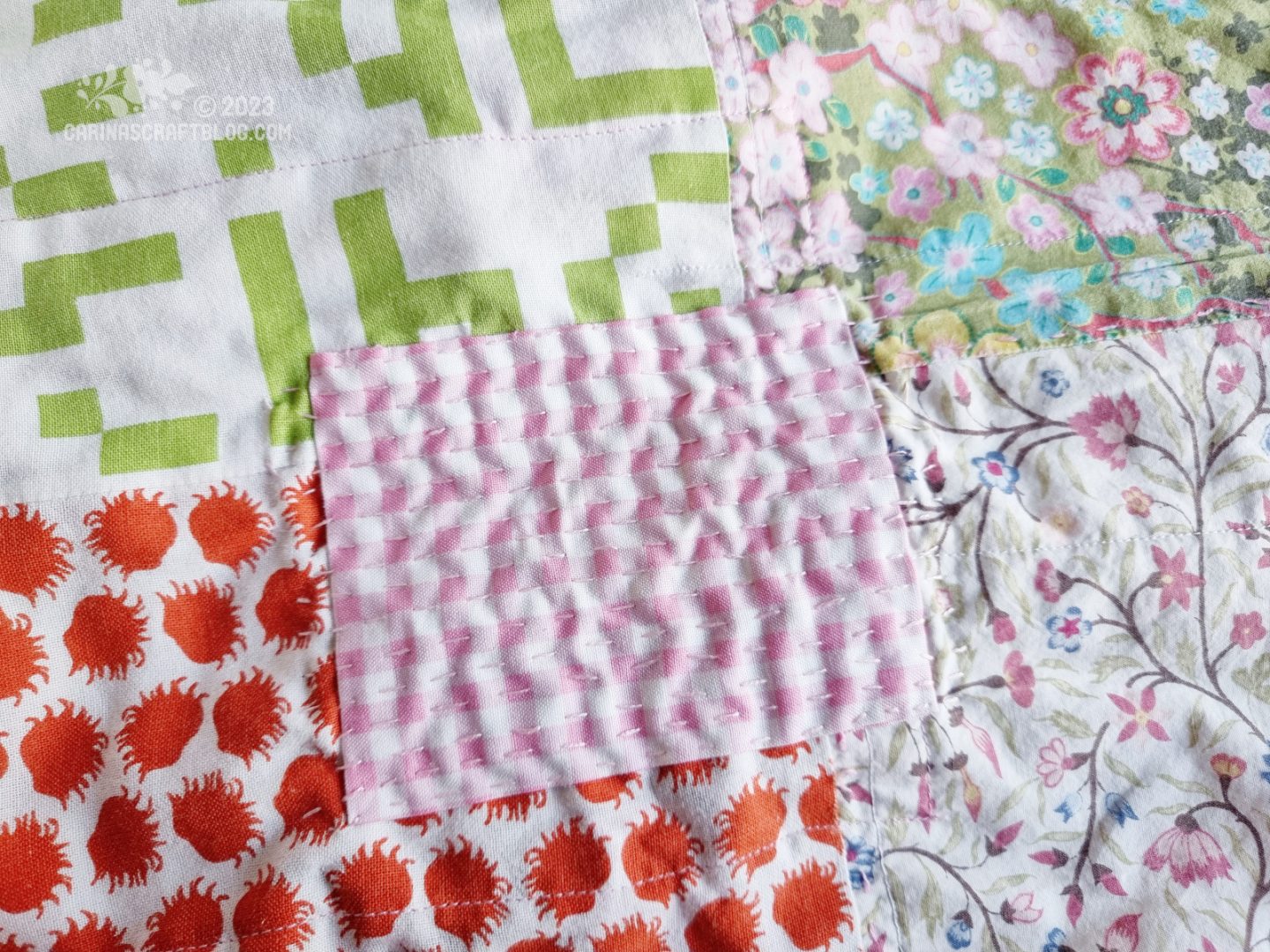 Close view of a mended patch on a patchwork blanket. The patch is pink and white checks with pink stitching across.