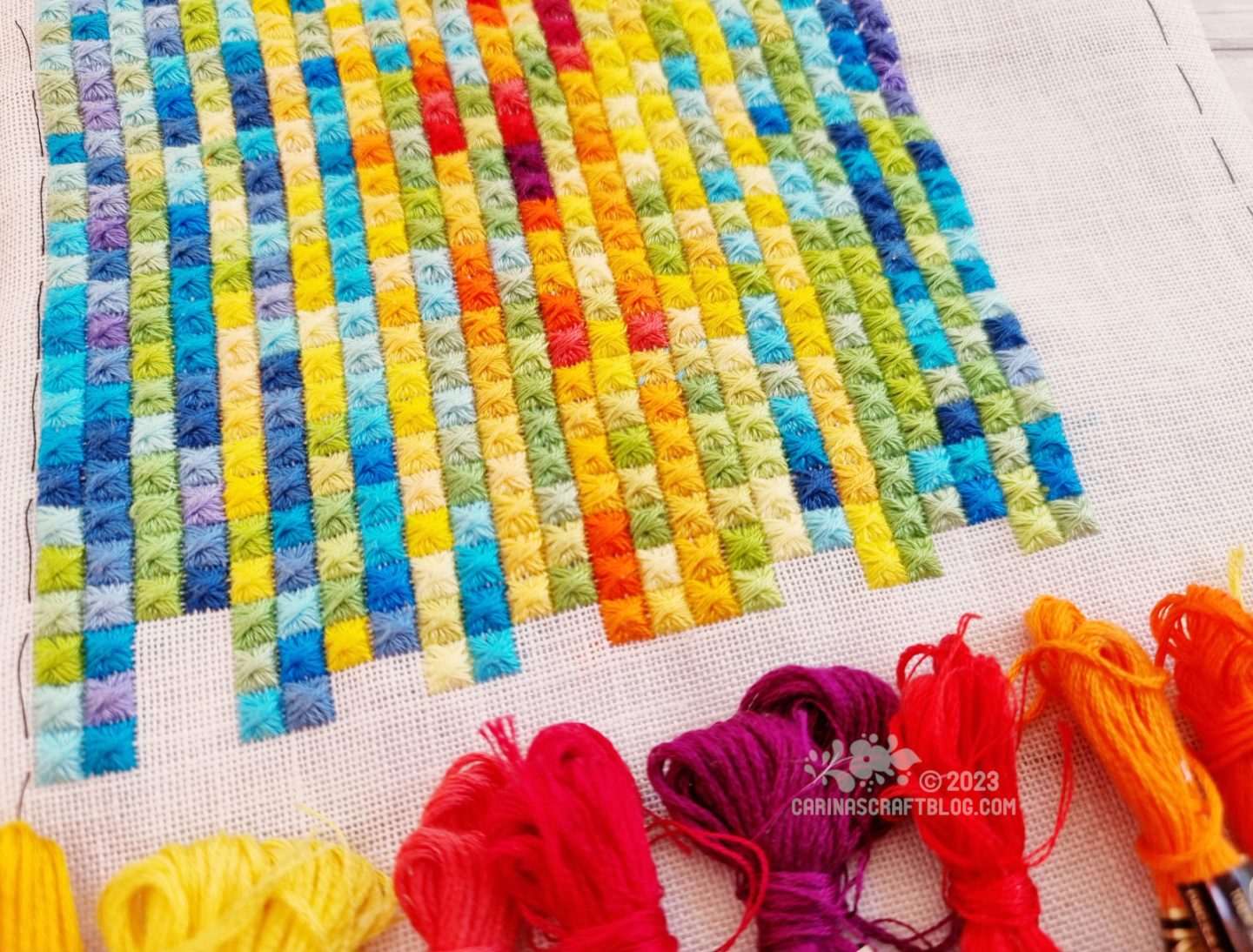 Close view of a  multicolour embroidery made up of rows and columns of square stitches.