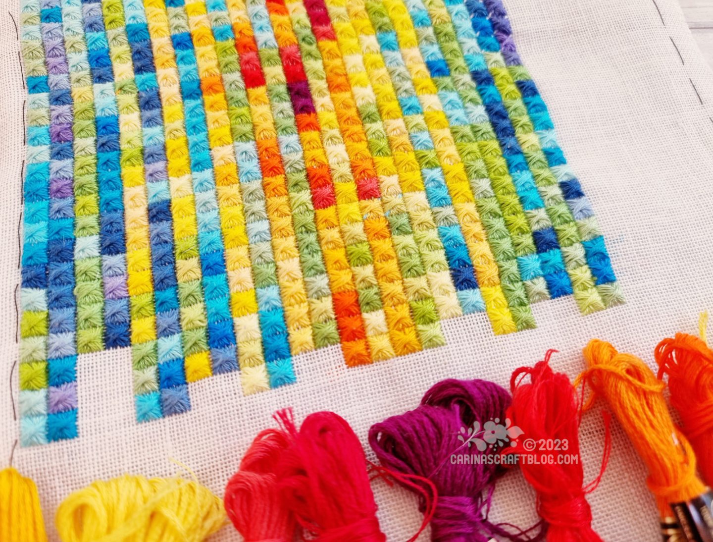 Close view of a multicolour embroidery made up of rows and columns of square stitches.