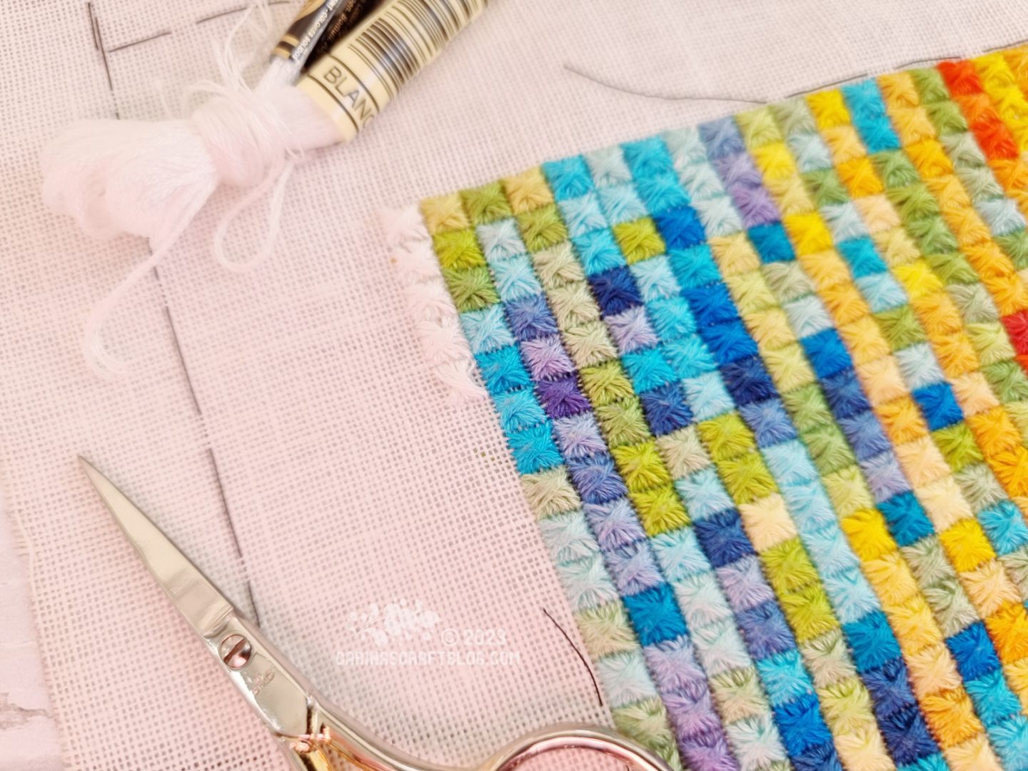 Closeup view of a  multicolour embroidery made up of rows and columns of square stitches. Along the top left corner are white square stitches.