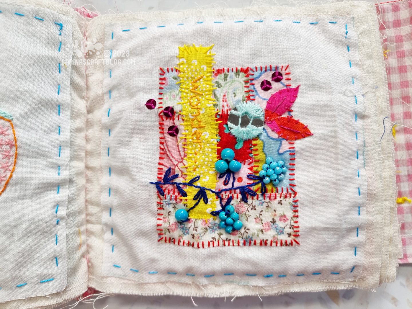 A page in a textile book. The background is unbleached cotton. On the fabric is appliqued a small patchwork with various stitches and beads and sequin embellishments. The main colours are pink, blues and yellow.