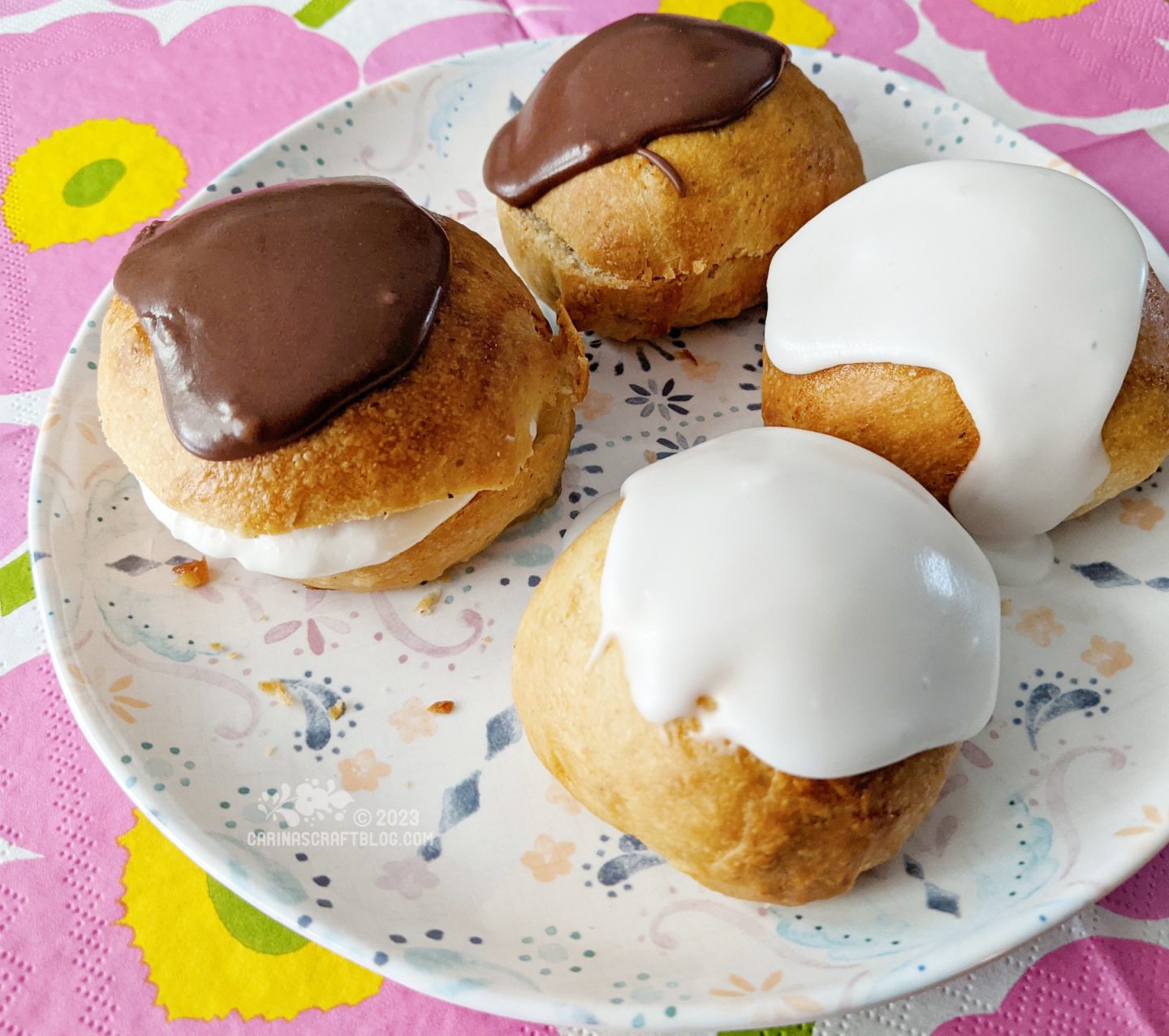 A white plate with a subtle pattern. On the plate are four buns decorated with icing sugar.
