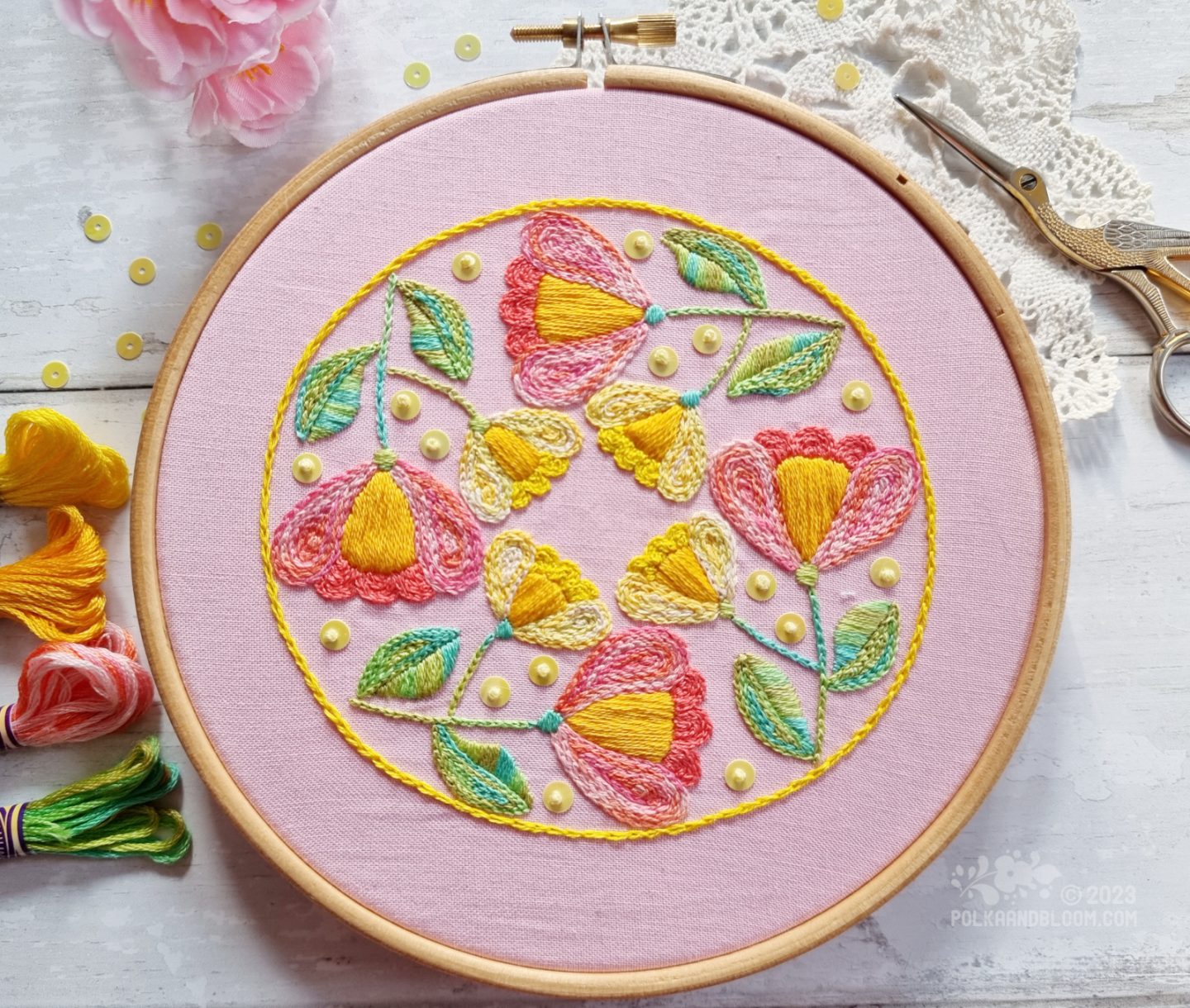 View from above of an embroidery hoop with light pink fabric. On the fabric is stitched a circular motif with a yellow outline and four folk art inspired tulips inside the outline.