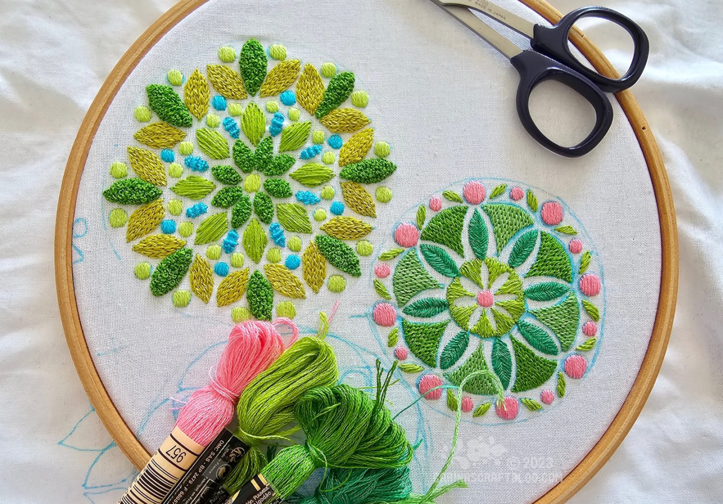 Two mandala inspired designs in green colours embroidered on white fabric framed in a wooden embroidery hoop.