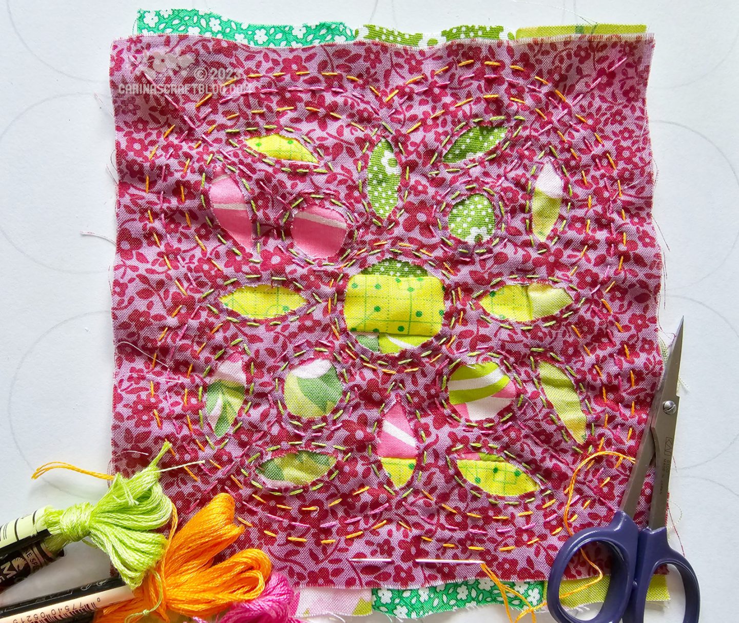 Leaf shaped holes have been cut in a square of dark magenta fabric to reveal a pink and green fabric piece underneath.