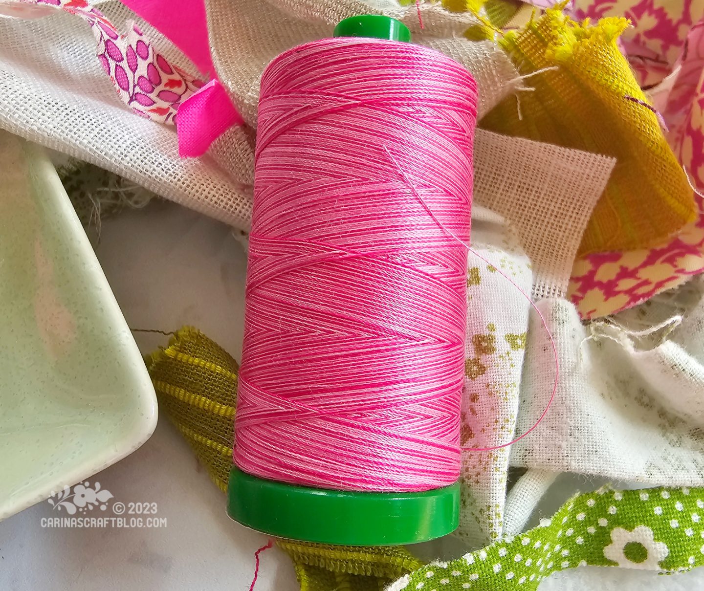 Close view of a spool of thread in a variegated pink colour. The spool itself is green.
