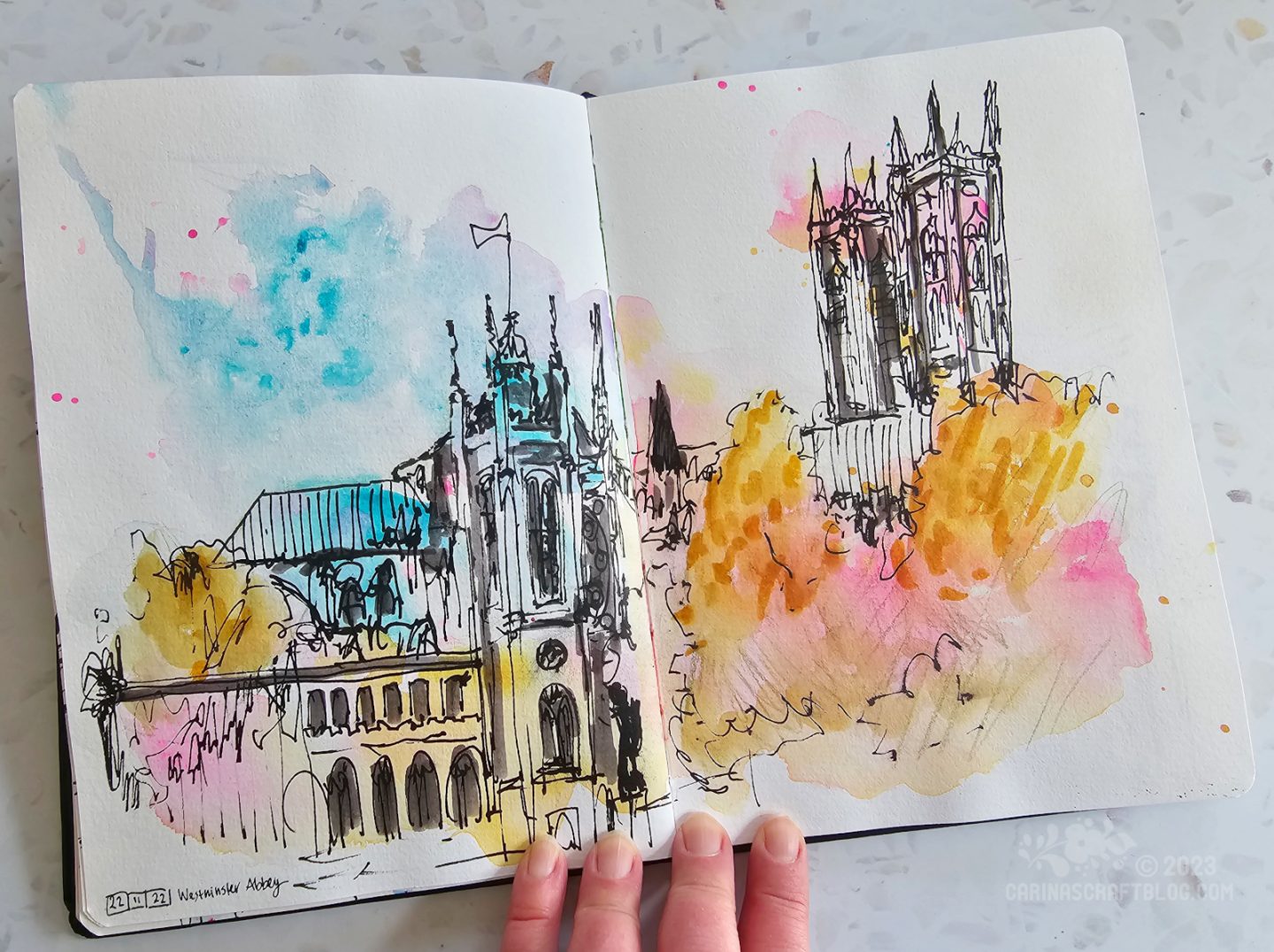 Photo of an open spread in a sketchbook. The spread shows a sketch of Westminster Abbey in London, drawn over pink, yellow and blue watercolour splashes.