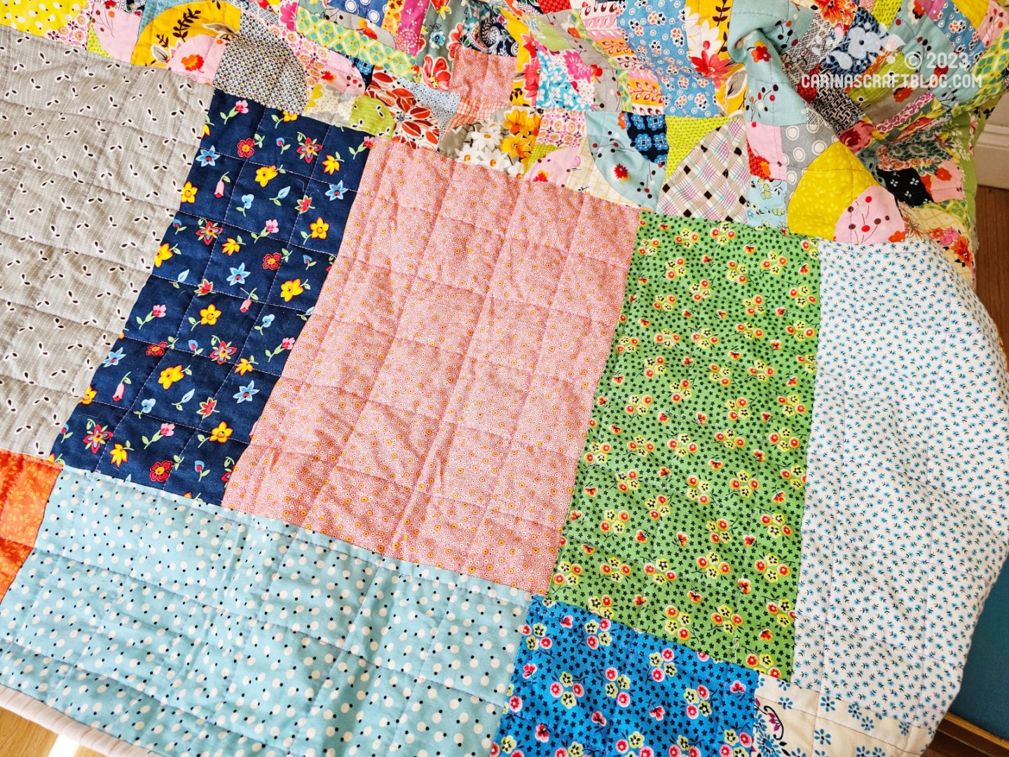 Near view of the back of a quilt, showing a section of large rectangular pieces of fabric in different prints and colours.