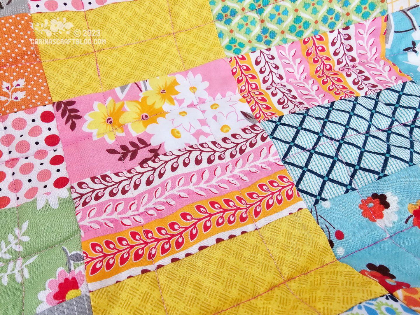 Close up of rectangular blocks on a quilt top. The blocks are in blue, green, pink and orange colours.