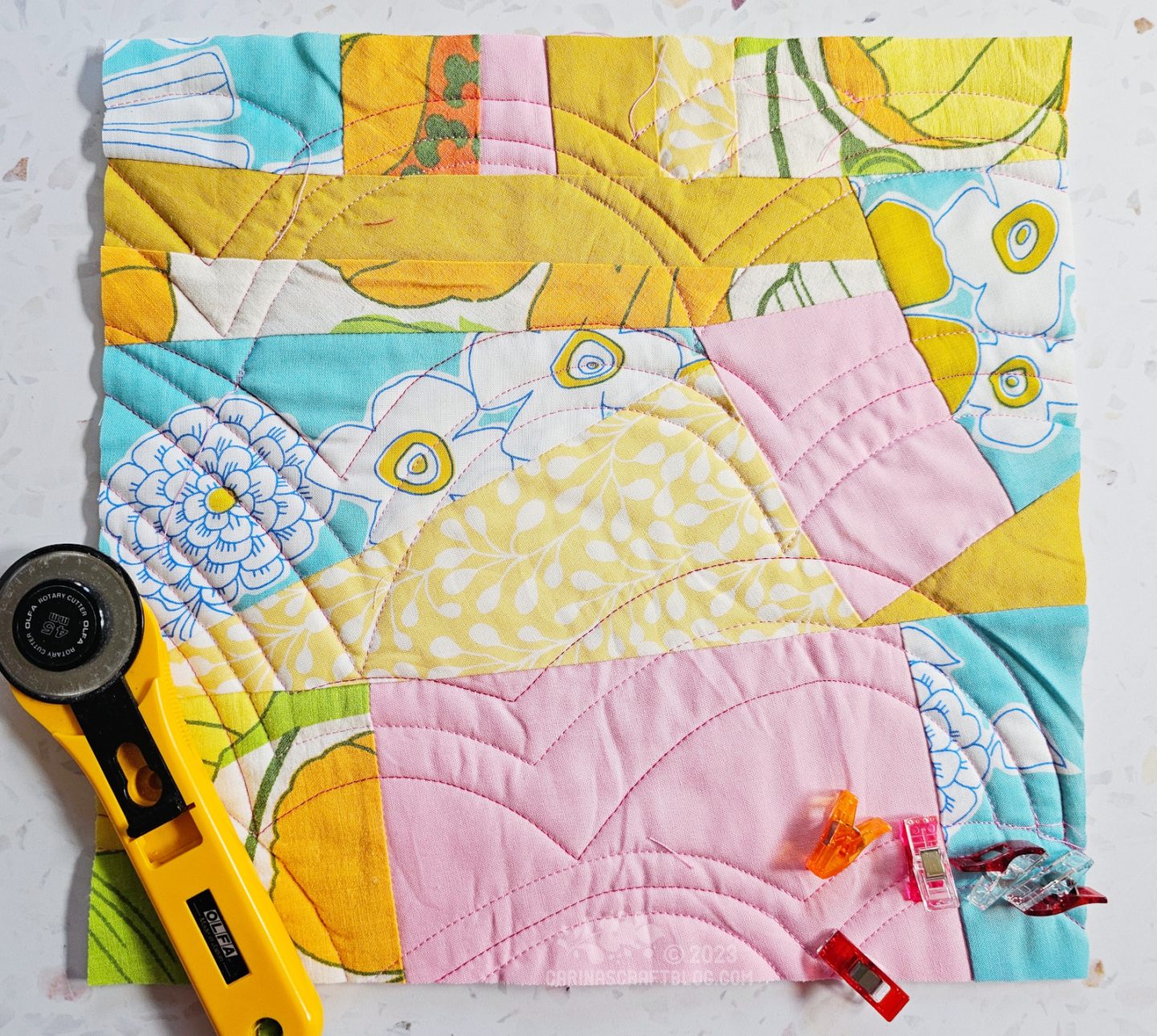 Small square quilt made of randomly shaped pieces of fabric in turquoise, pink and yellow colours.