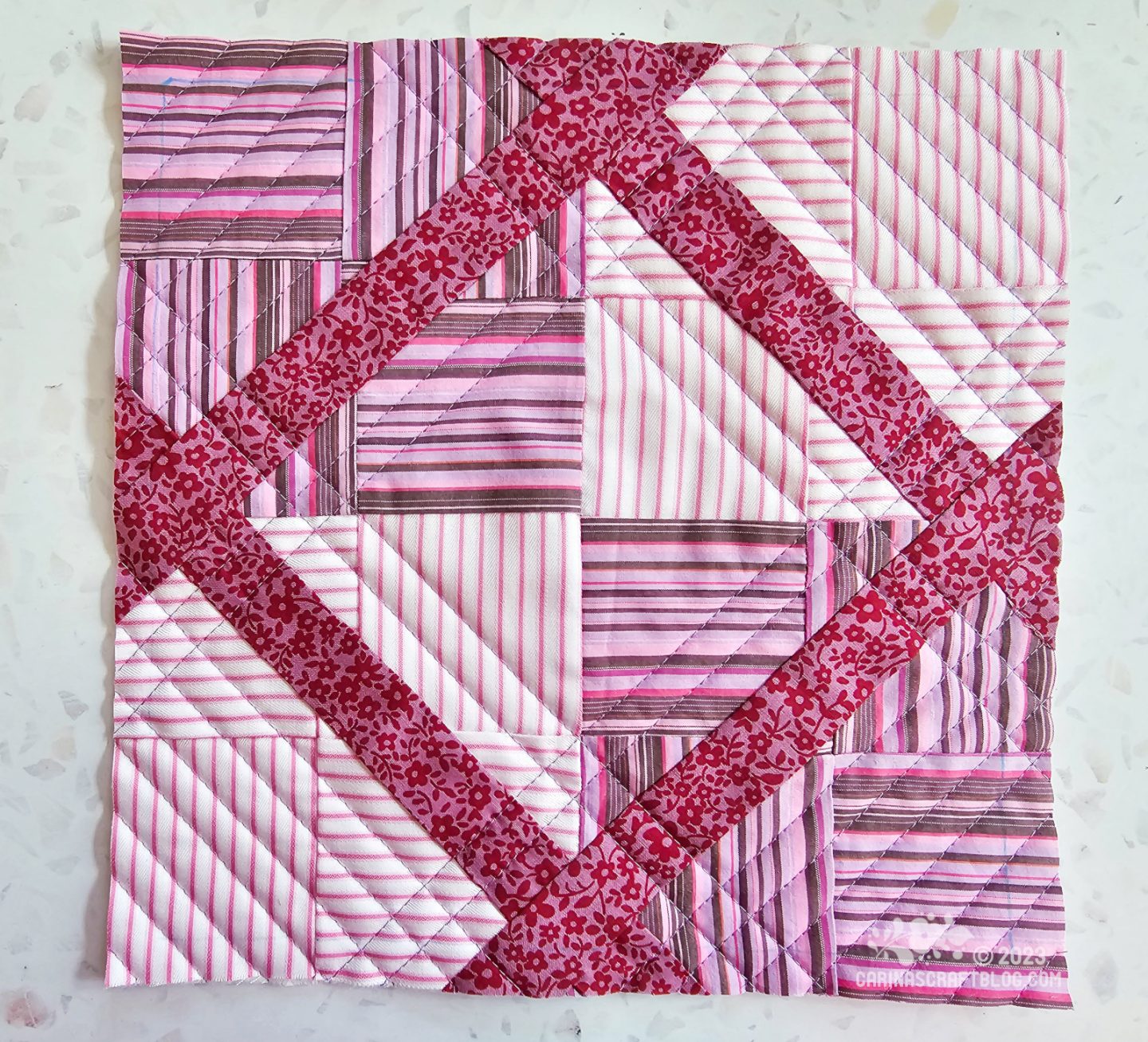A small square quilt made up of four striped squares. The corner sections have been separated from the centre and diagonal strips have been inserted.