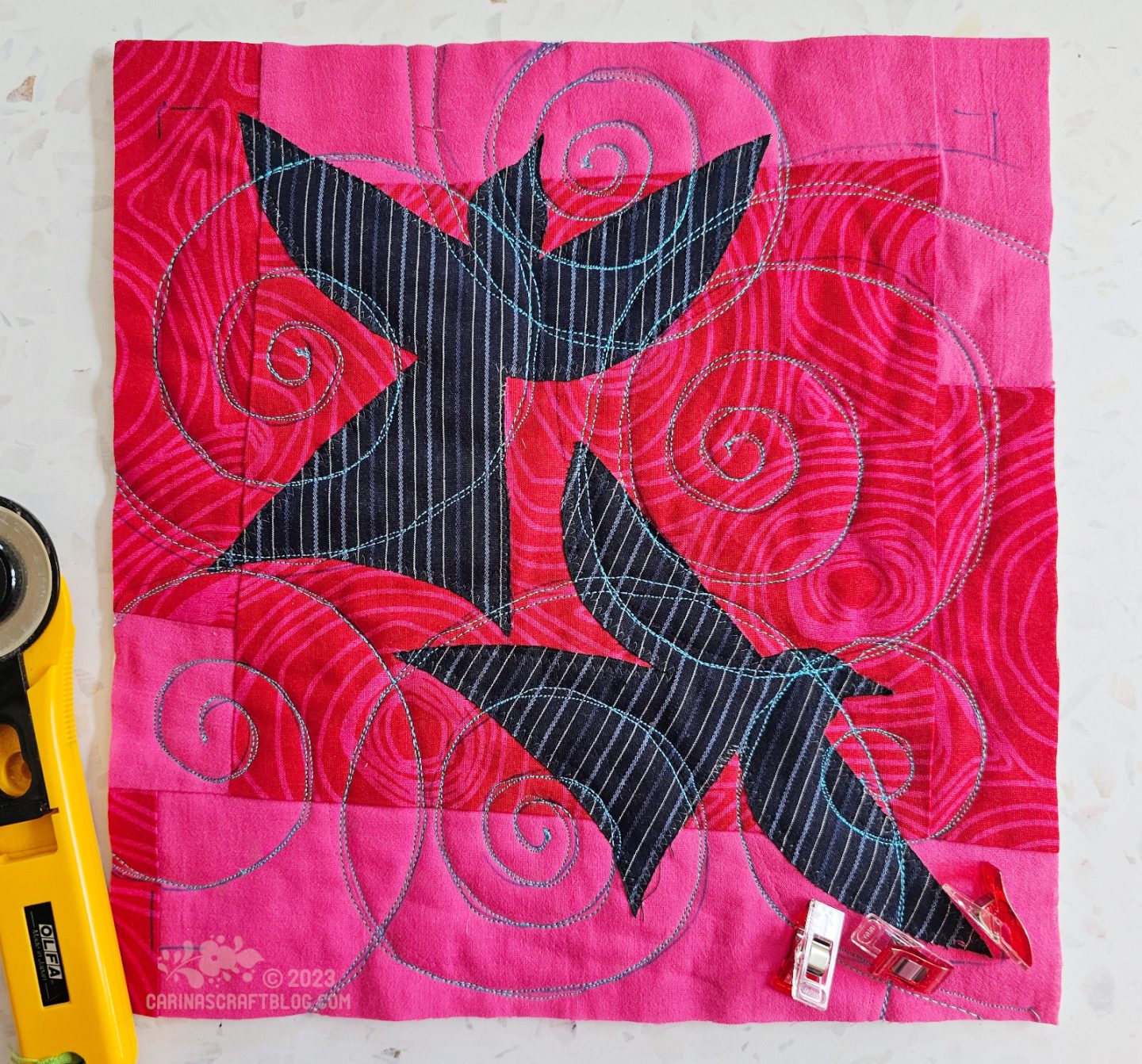 A small square quilt with a randomly pieced back in two hot pink colours with two dark blue birds appliquéd on top.