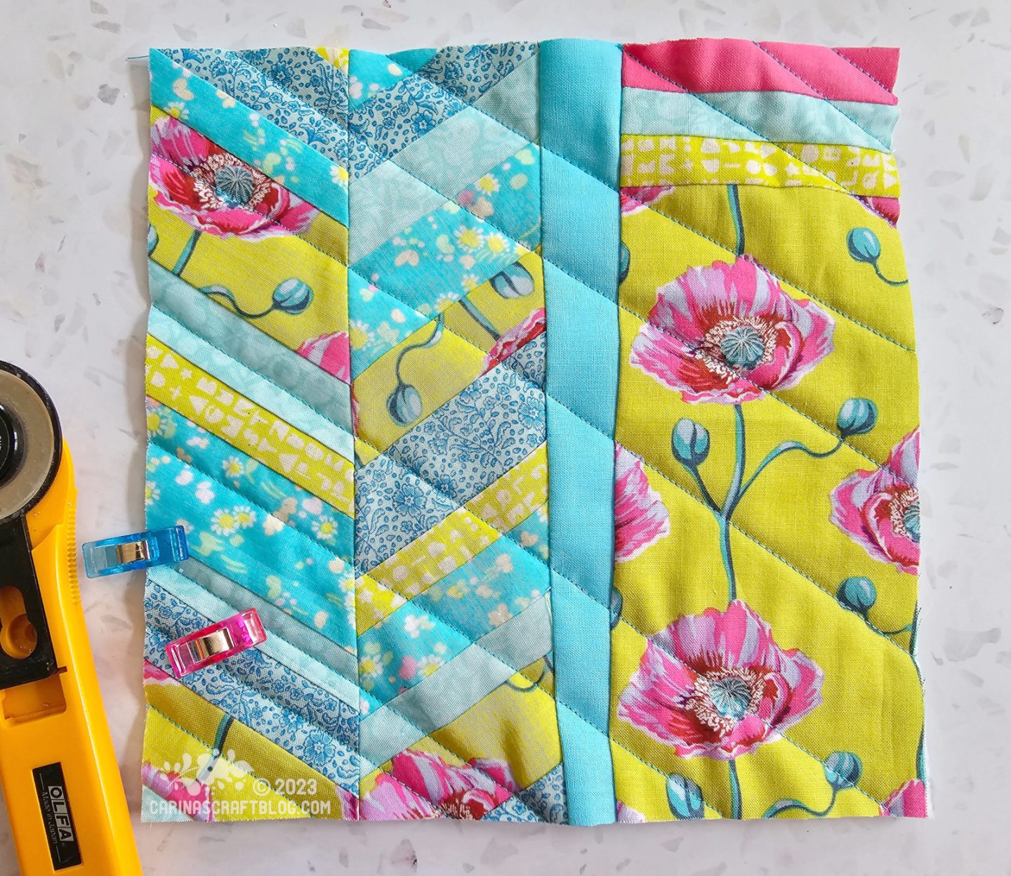Small square quilt made up of a herringbone pattern with narrow strips in lime green and aqua fabrics on one half. The other half of the quilt is a strip of solid aqua colour fabric running vertically and a rectangle piece of lime green fabric with a print of pink poppies.