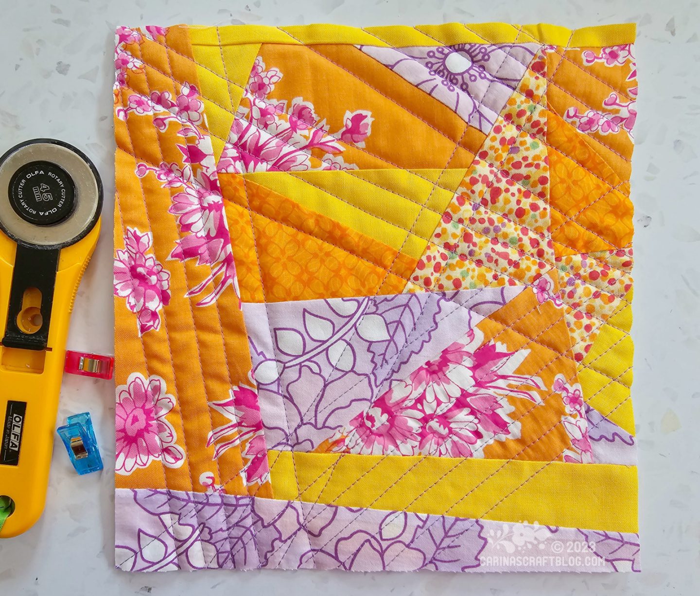 Small square quilt made of differently shaped and sized triangles in yellow, purple and orange colours.