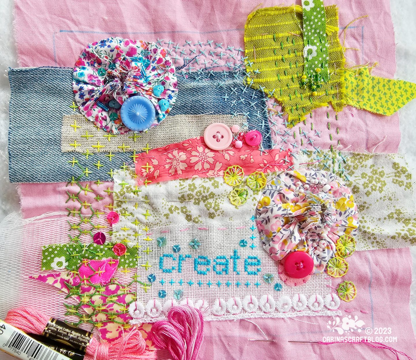 Close overhead view of a slow stitching piece with many different scraps of fabric, buttons, and embroidery on a pink fabric background.
