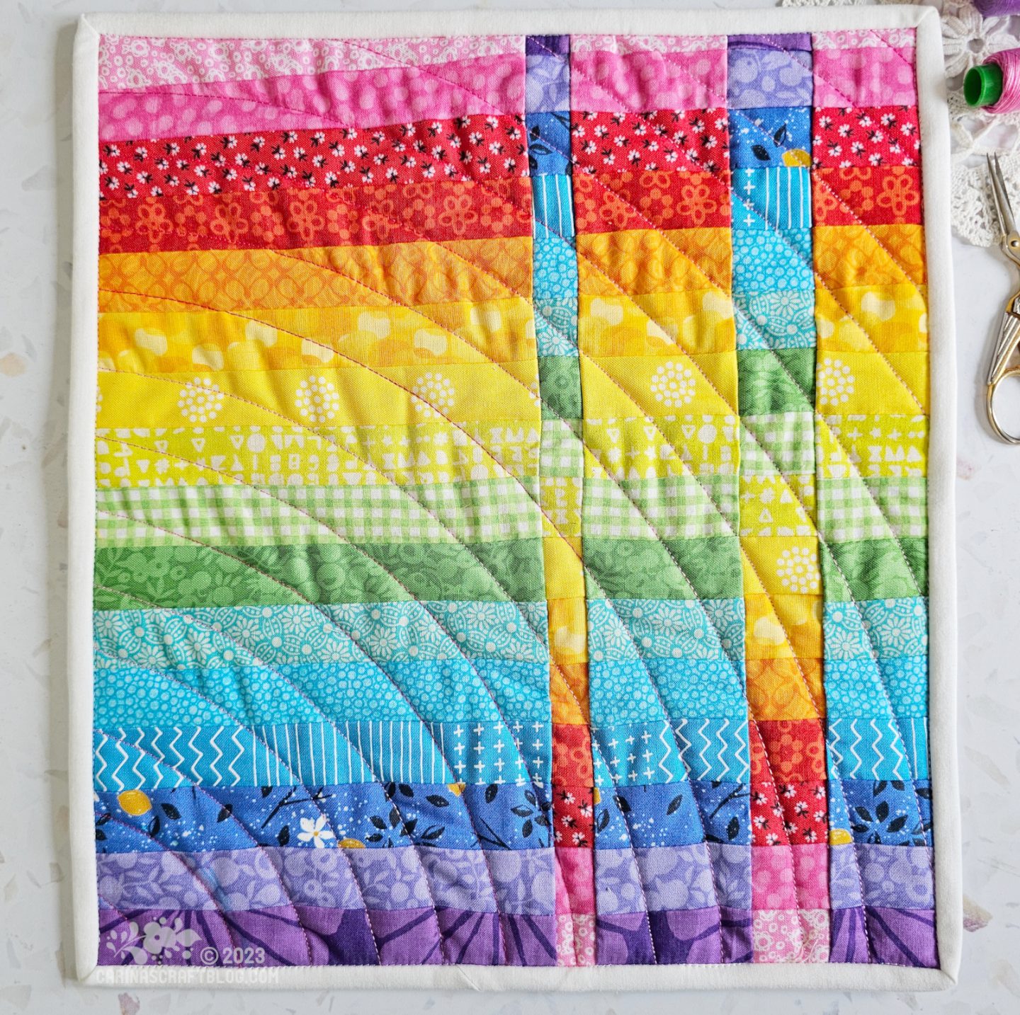 View from above of a mini quilt. quilt is made of horizontal strips of colour in rainbow colour order from pink at the top to purple at the bottom. Inset with two strips of the same piecing going in the opposite colour direction.