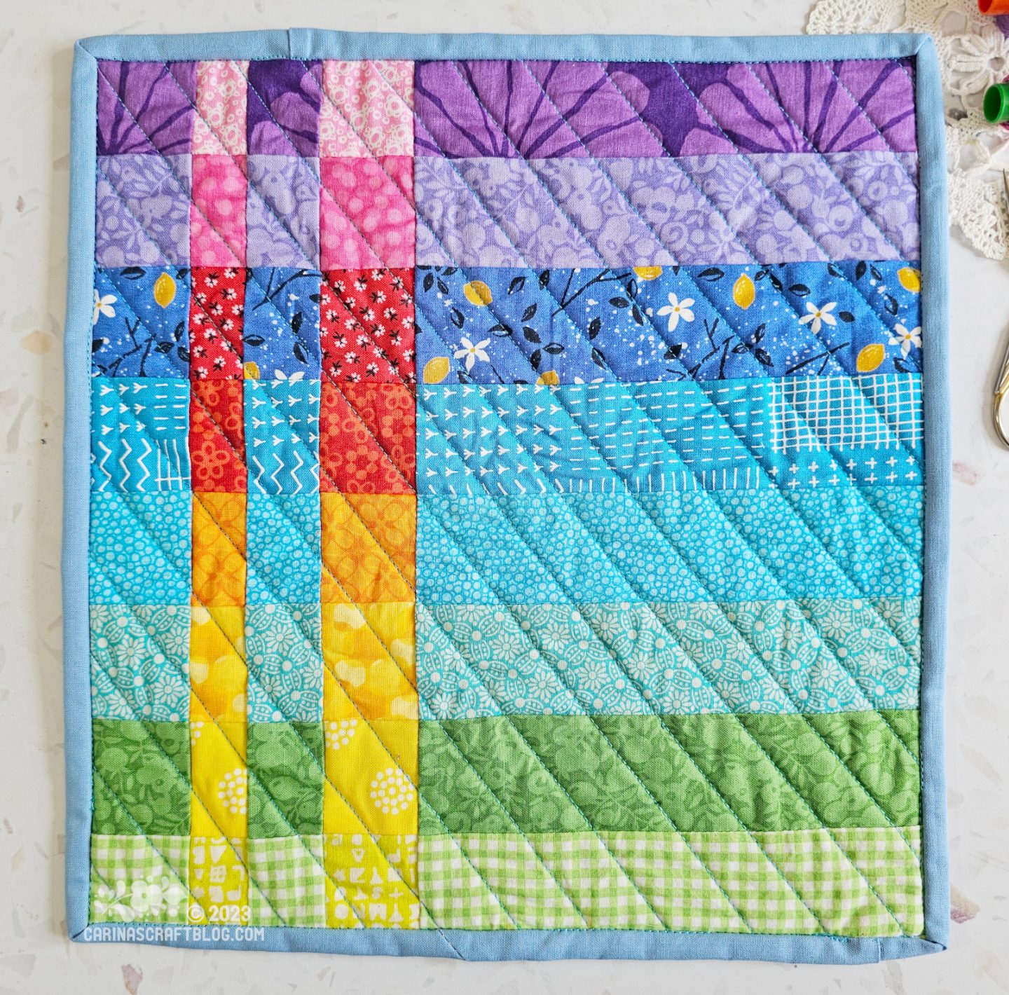 View from above of a mini quilt. quilt is made of horizontal strips of cool colours in rainbow colour order from purple at the top to green at the bottom. Inset with two strips of warm colours.