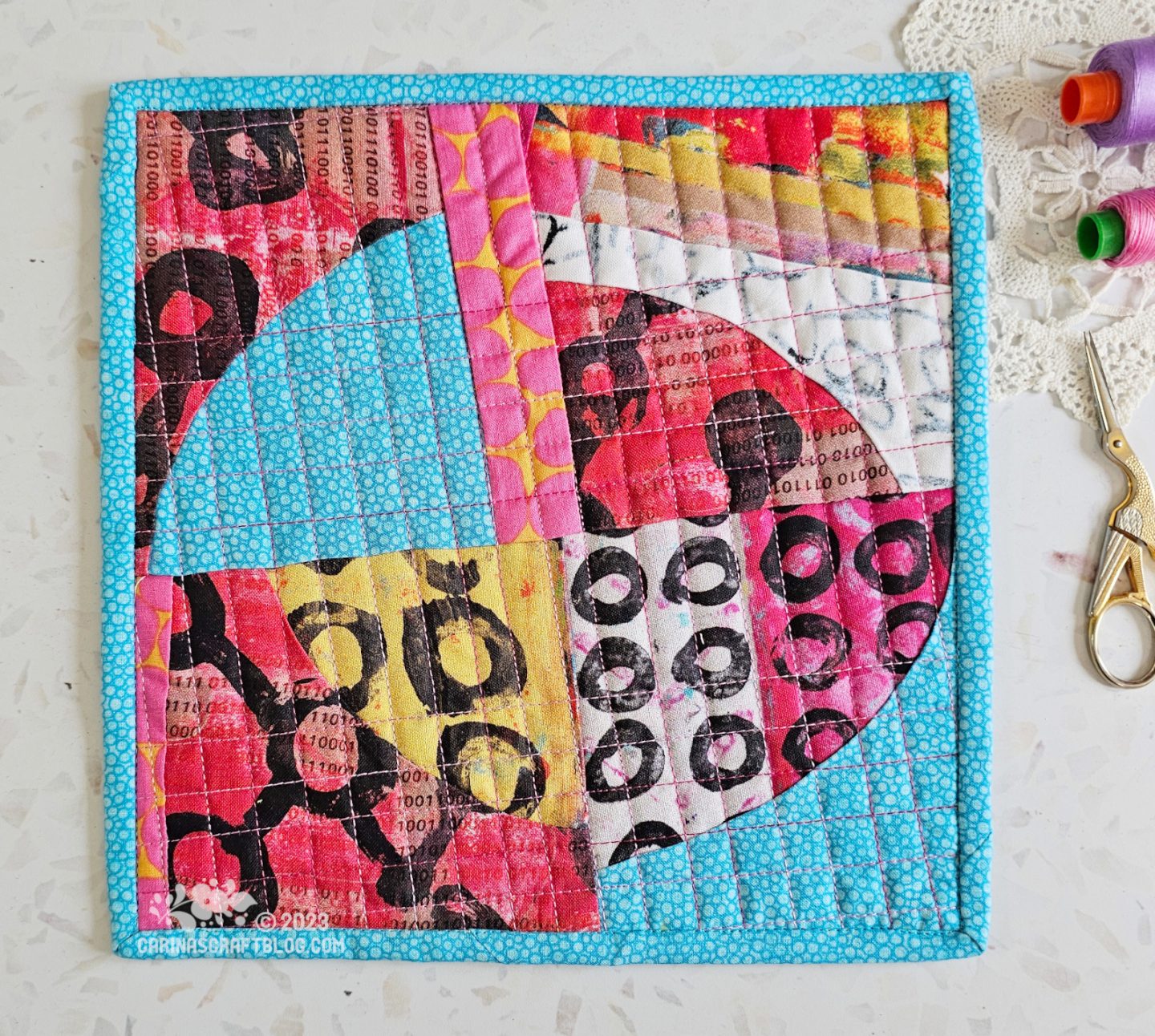 View from above of a mini quilt. Quarter circles pieced in a random way in blue, pink and yellow colours.