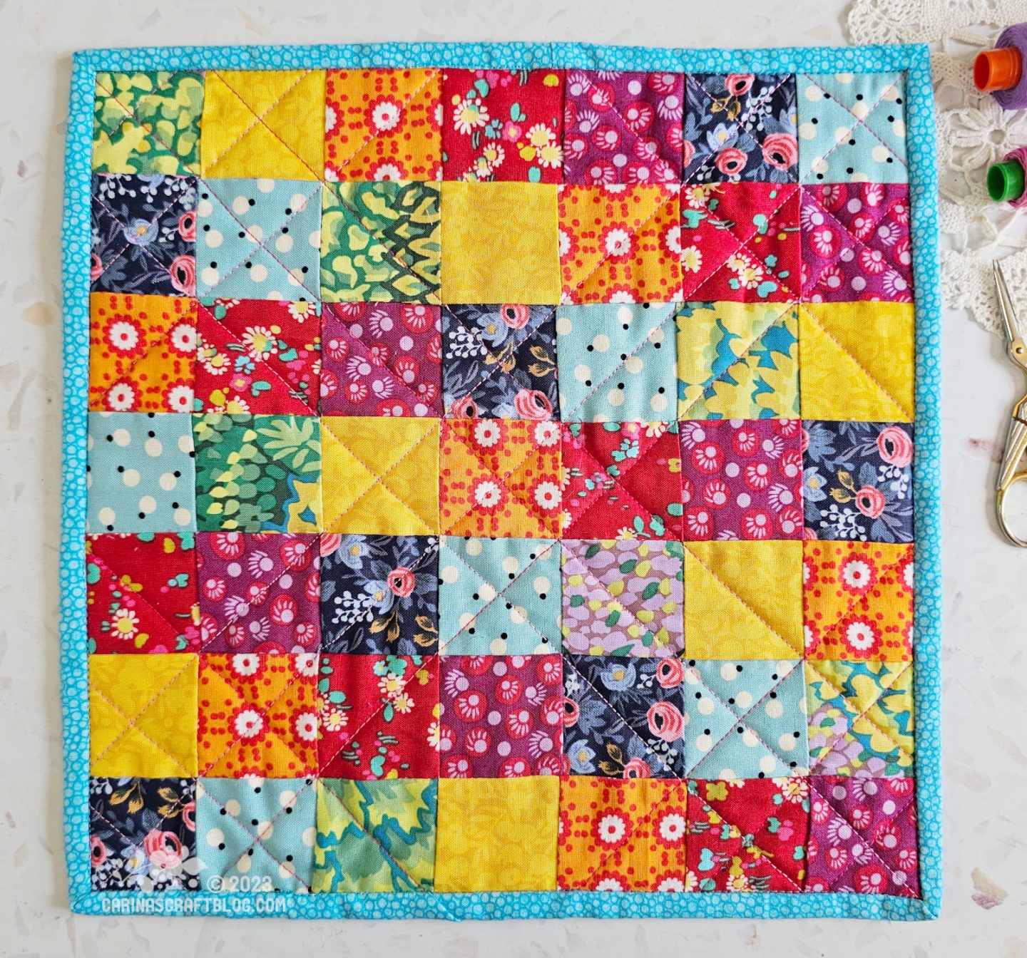 View from above of a mini quilt. The quilt is made of squares in rainbow colours pieced in a random pattern.