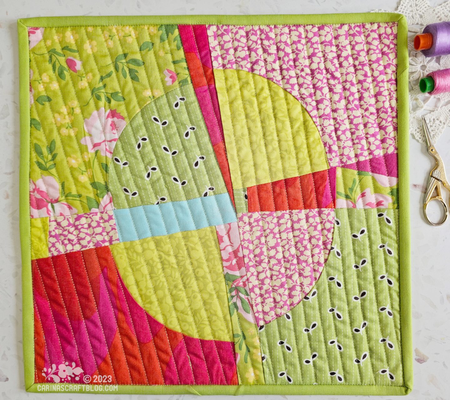 View from above of a mini quilt. Quarter circles pieced in a random way in pink, green and red with a blue strip.