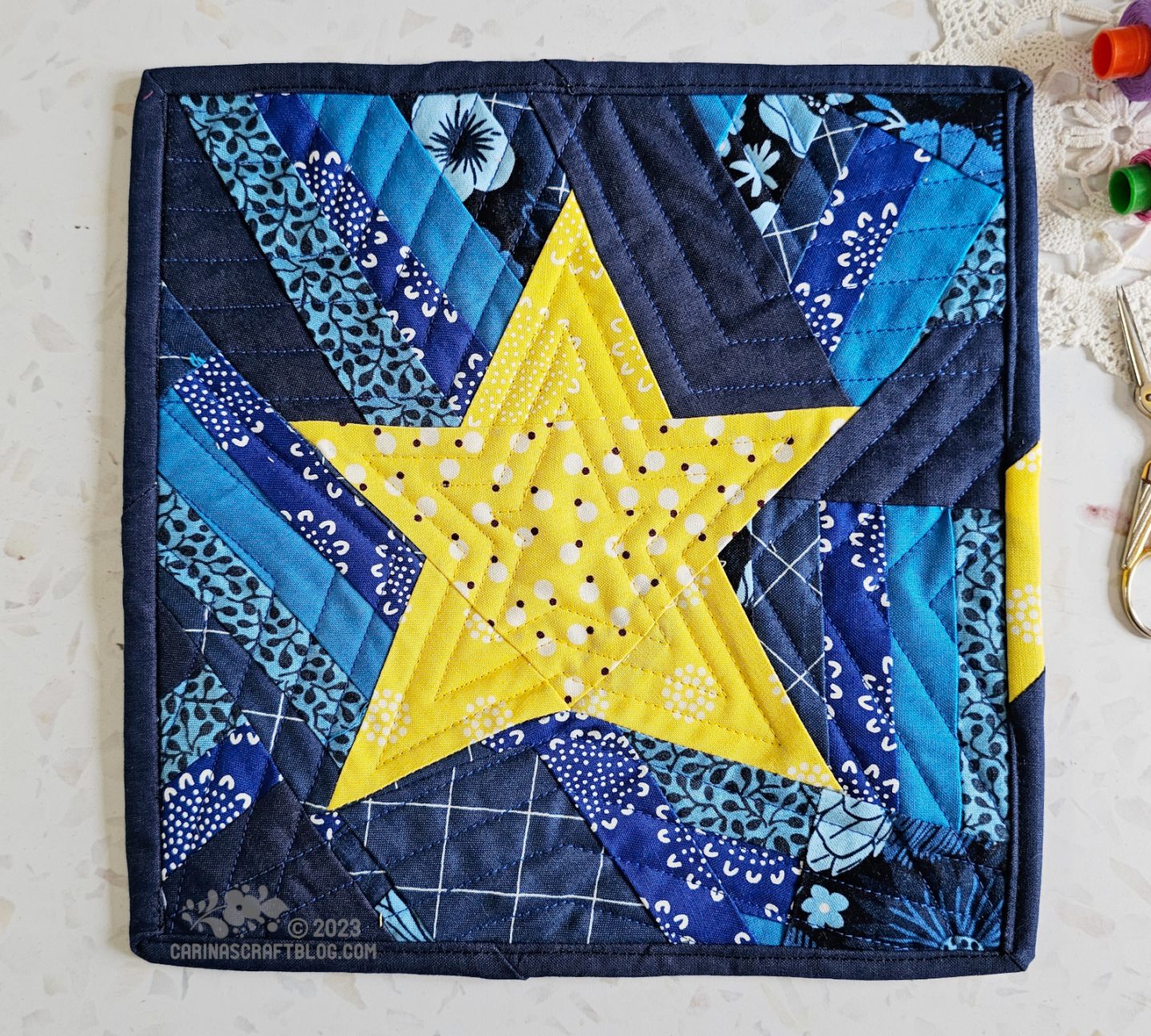 View from above of a mini quilt. Randomly pieced five pointed star on a dark blue background.