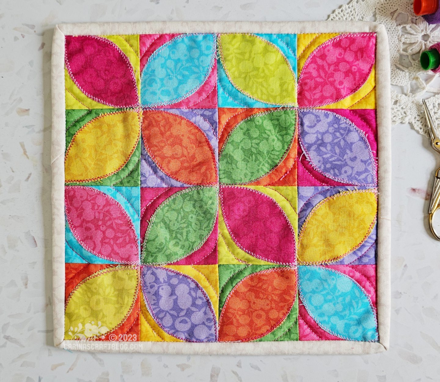 View from above of a mini quilt. 16 patch block with orange peels appliquéd on top. In happy colours: pink, yellow, orange, purple, green, lime green, turquoise.