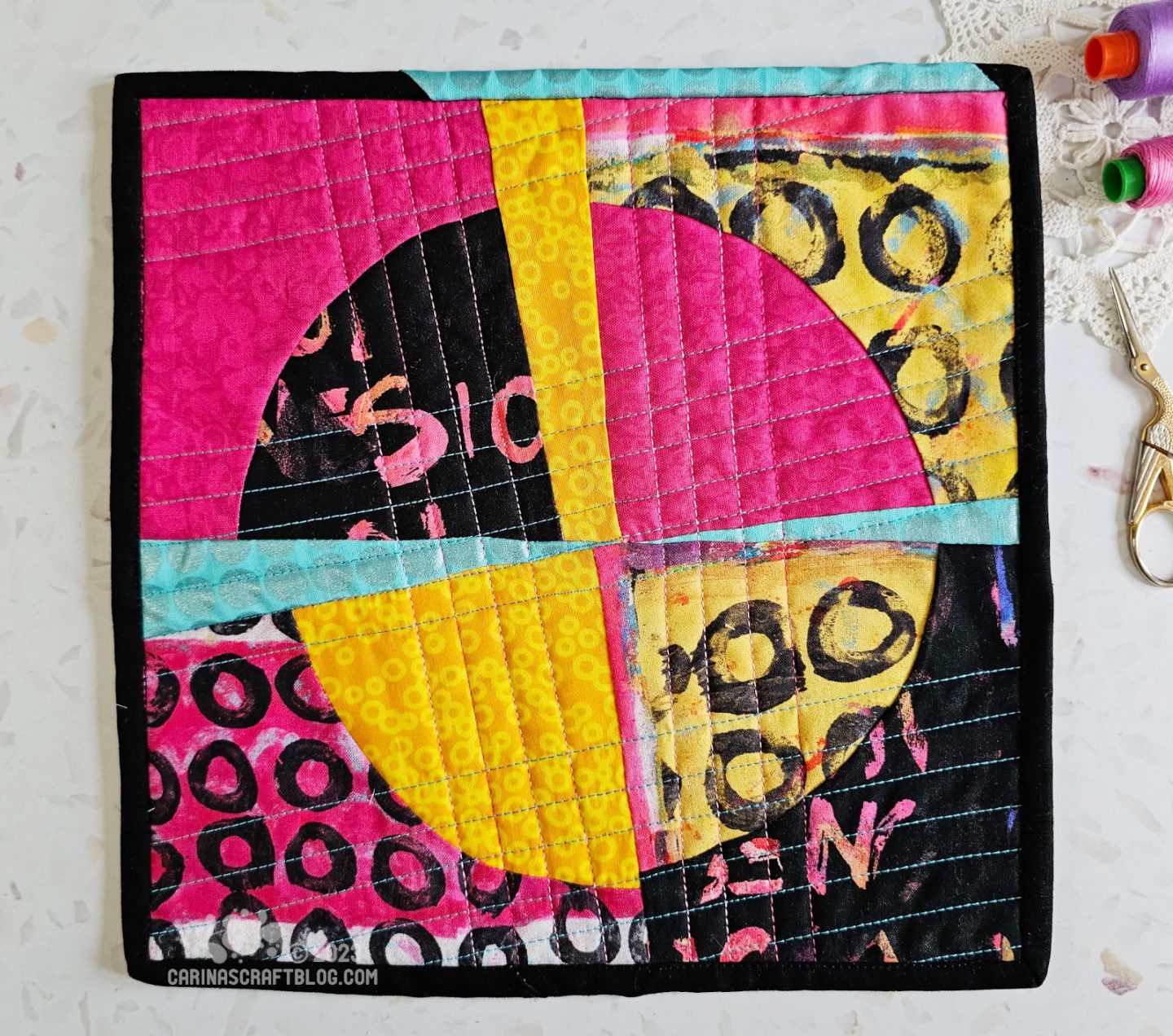 View from above of a mini quilt. Quarter circles pieced in a random way in hot pink, black and yellow.