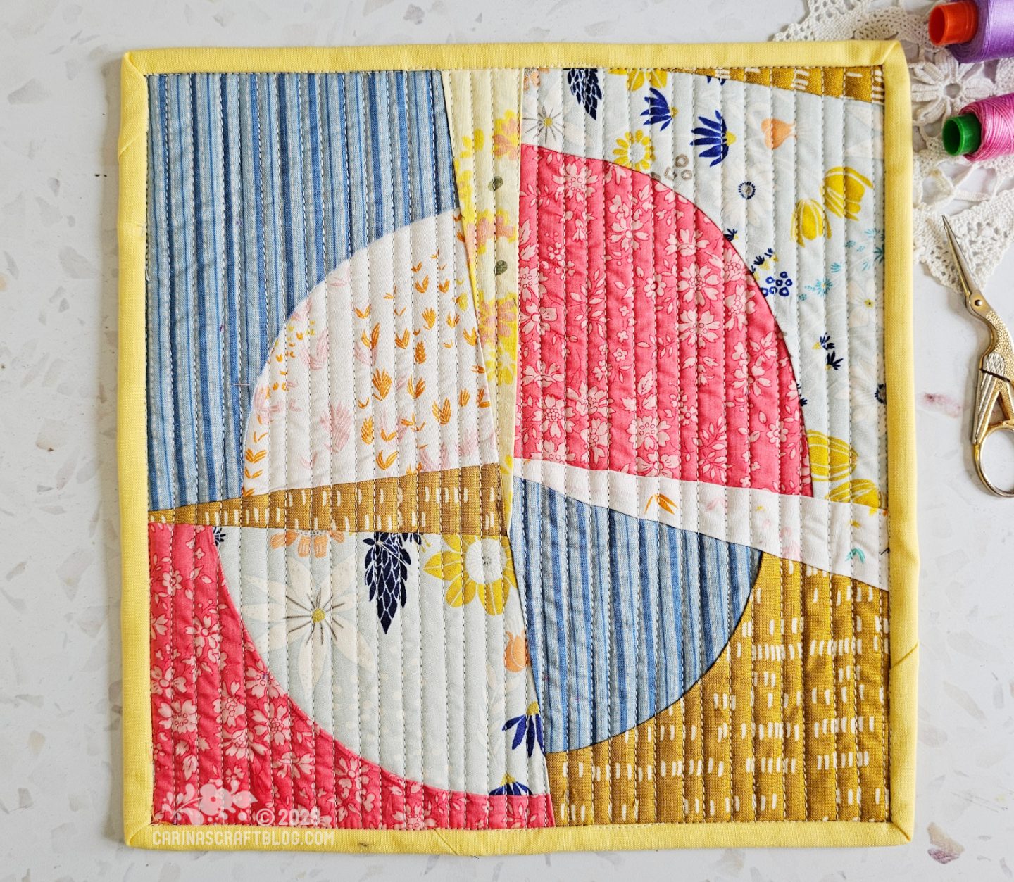 View from above of a mini quilt. Quarter circles pieced in a random way in blue, light blue, pink and mustard yellow.