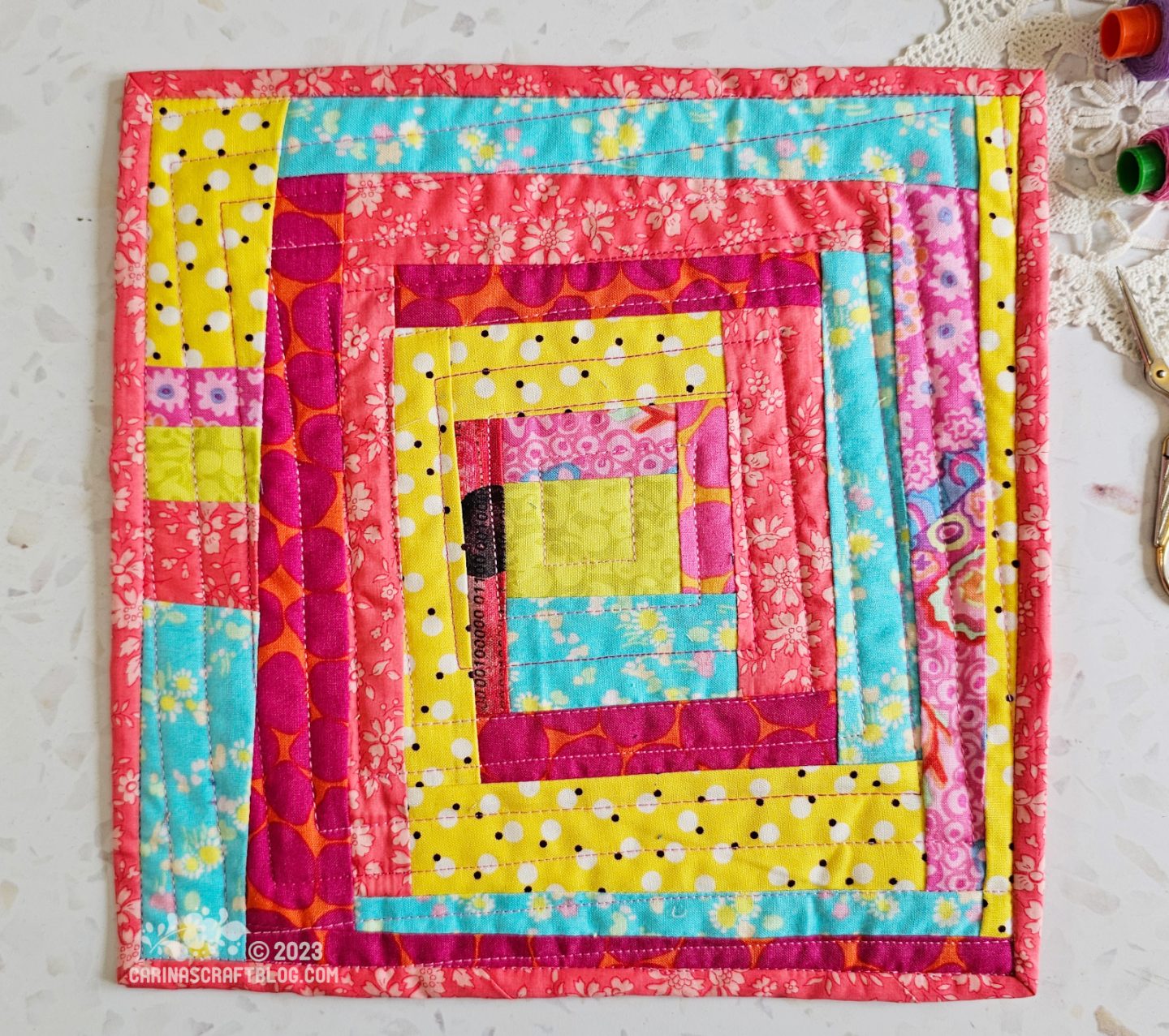 View from above of a mini quilt. Wonky log cabin design worked in yellow, pink and turquoise colours.