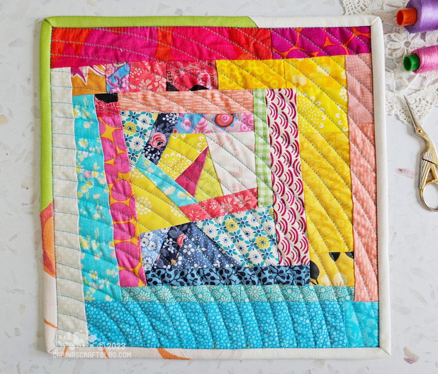 View from above of a mini quilt. Wonky log cabin design mainly worked in yellow, pink and blue colours.