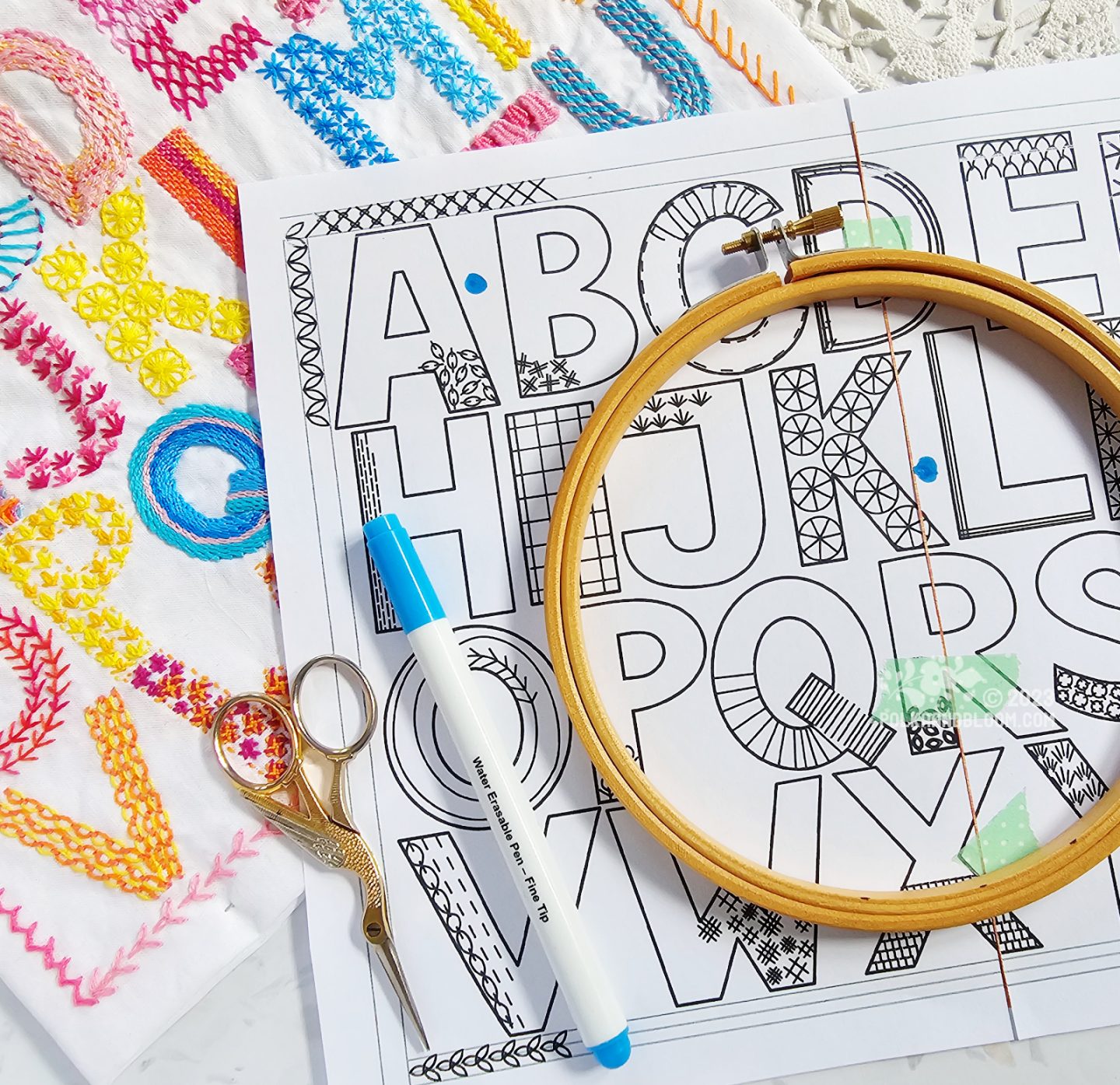 Overhead view of a rectangle of white fabric embroidered with the letters of the English alphabet plus the ampersand.