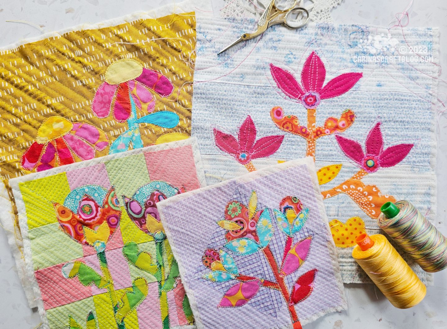 Overhead view of four small quilted pieces of fabric with flower designs appliquéd on. 