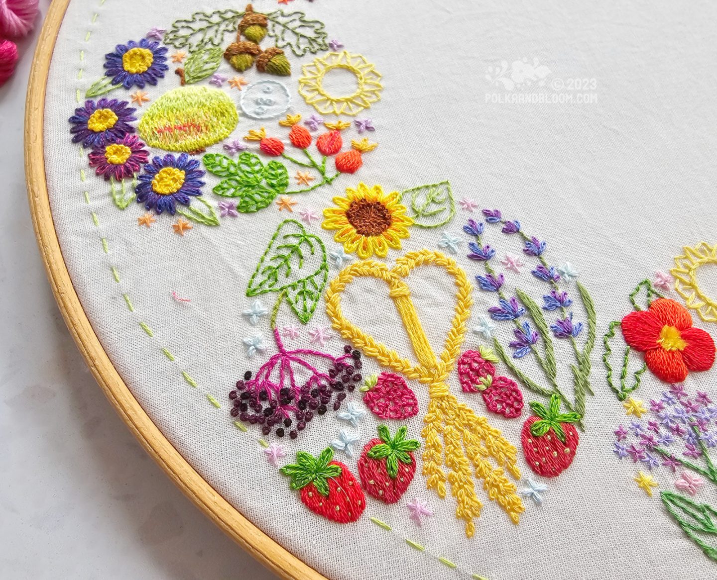 Closeup of a circular embroidery with strawberries, lavender, elderberries and sunflower.