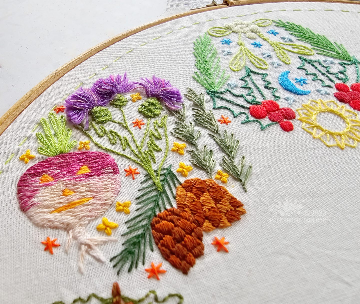 Closeup of a circular embroidery with pine cones, thistles and a carved turnip.